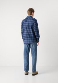 Camisa de franela de cuadros azul para hombre con cuello abotonado, que presenta tonos de azul marino y azul claro, combinada con jeans azul claro.