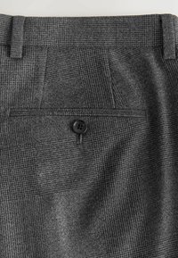 Grå ternede bukser med et subtilt mønster, der har en baglomme og sort knapdetalje. Stoffet har en glat tekstur.