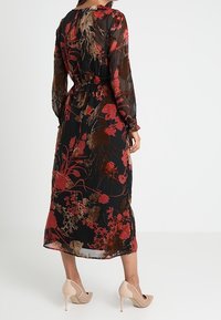 Sort blomster midi kjole med lange ærmer, prydet med mønstre af røde og brune blomster; parret med nude højhælede sko.