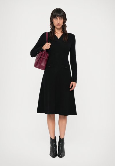 Musta neulottu mekko pitkillä hihoilla, tiukas yläosa, levenevä hameosa ja kaksi taskua. Asusteina pieni burgundinpunainen käsilaukku ja mustat nilkkurit hopeisilla niiteillä.