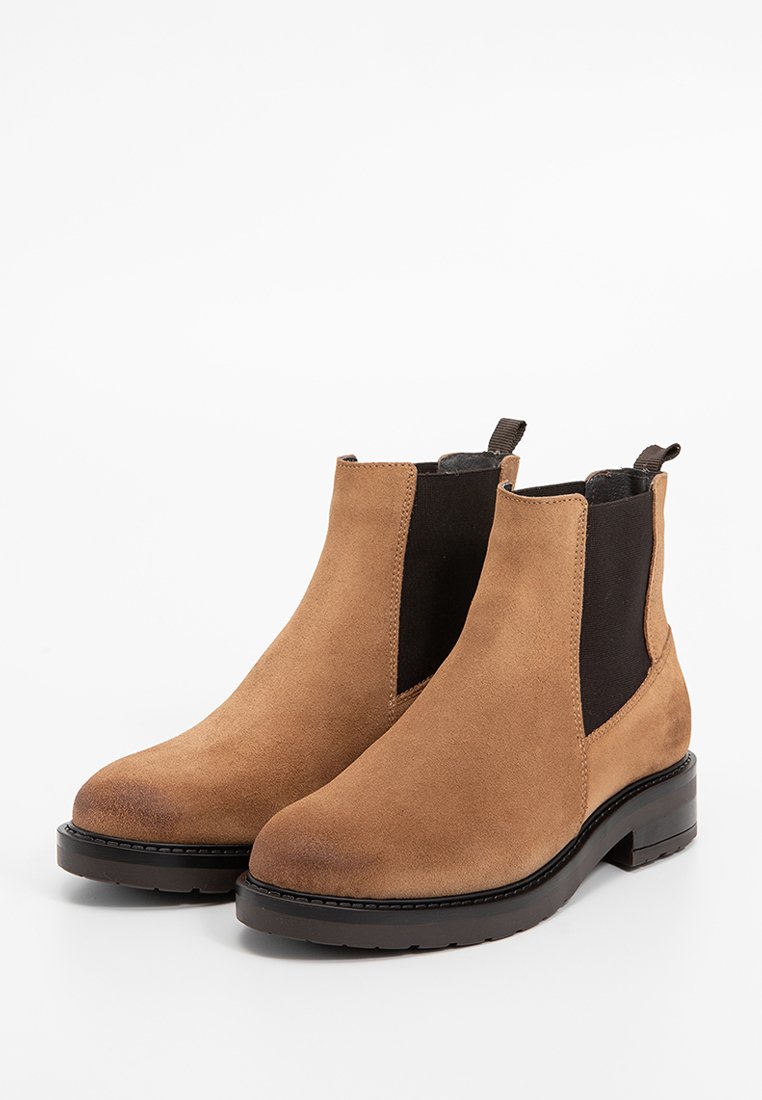 Botas Chelsea de ante marrón con paneles laterales elásticos, punta redondeada y suela de goma texturizada. Cuenta con una tirador para facilitar su uso.