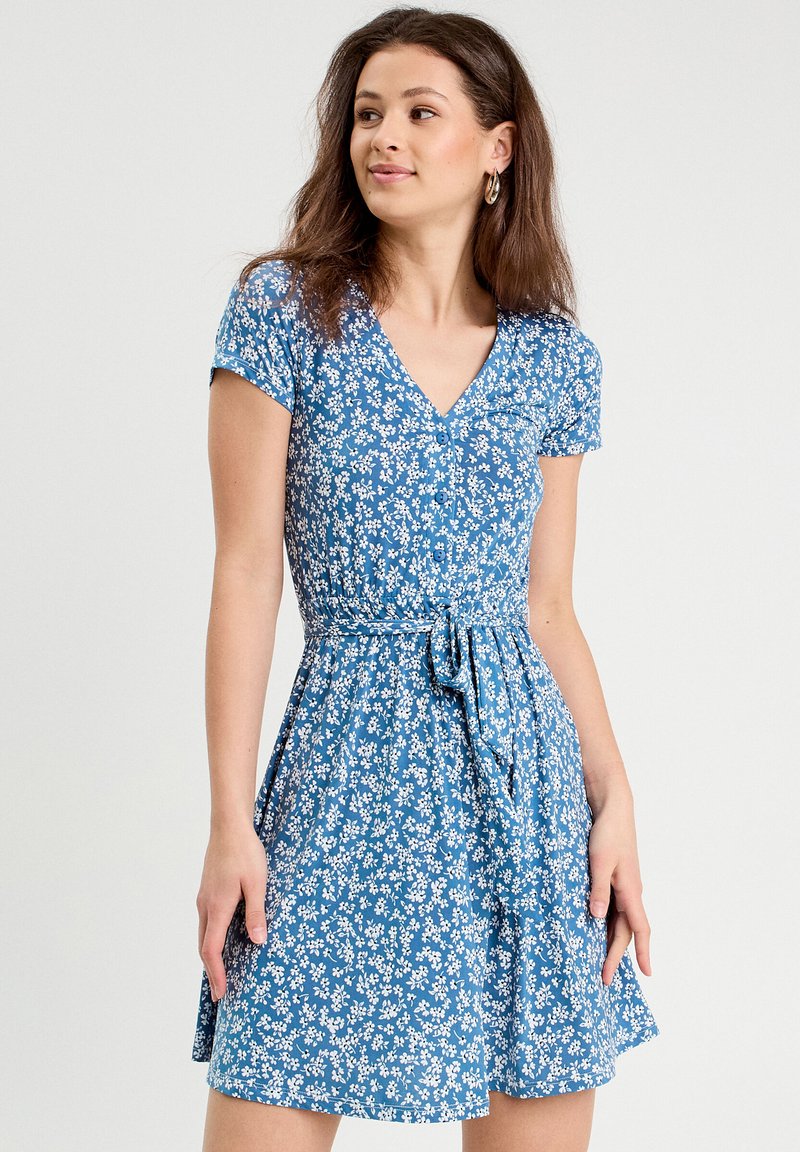 Vestido floral azul con mangas cortas, escote en V, cintura ceñida y detalle de lazo en la cintura. Hecho de tela ligera con una textura suave.