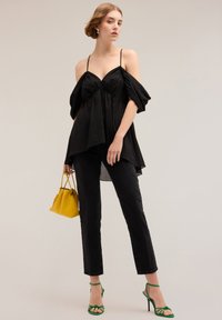 Top nero con spalle scoperte e maniche a sbuffo, abbinato a jeans neri, tacchi verdi con cinturini e una borsa gialla. Tessuto morbido e vestibilità morbida.