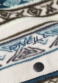 Koc z polaru o geometrycznym wzorze w kolorze niebieskim, szarym i kremowym; posiada wyszywane logo "ONEILL" oraz okrągłą czarną metkę.