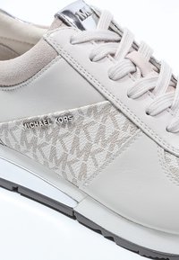 Baskets en cuir blanc avec accents en daim, motif texturé sur le côté, lacets beige et logo métallique sur le talon.