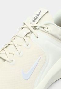 Ανοιχτό μπεζ αθλητικό παπούτσι με υφαντό επάνω μέρος, λευκές λεπτομέρειες και έντονο λογότυπο Swoosh. Διαθέτει κορδόνια και μαλακή σόλα.