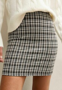 Black and white checkered mini skirt worn with a white knit sweater, showing waist to mid-thigh with one hand visible at side.