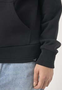 Schwarzer Pullover mit Kängurutasche, gerippten Bündchen und Saum, aus weichem Stoff mit subtiler Textur.
