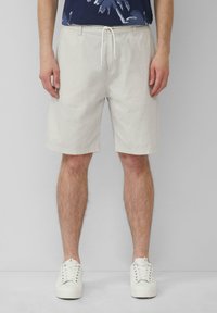 Hellgraue gemusterte Shorts mit elastischem Bund, Kordelzug und Seitentaschen, kombiniert mit weißen Turnschuhen.