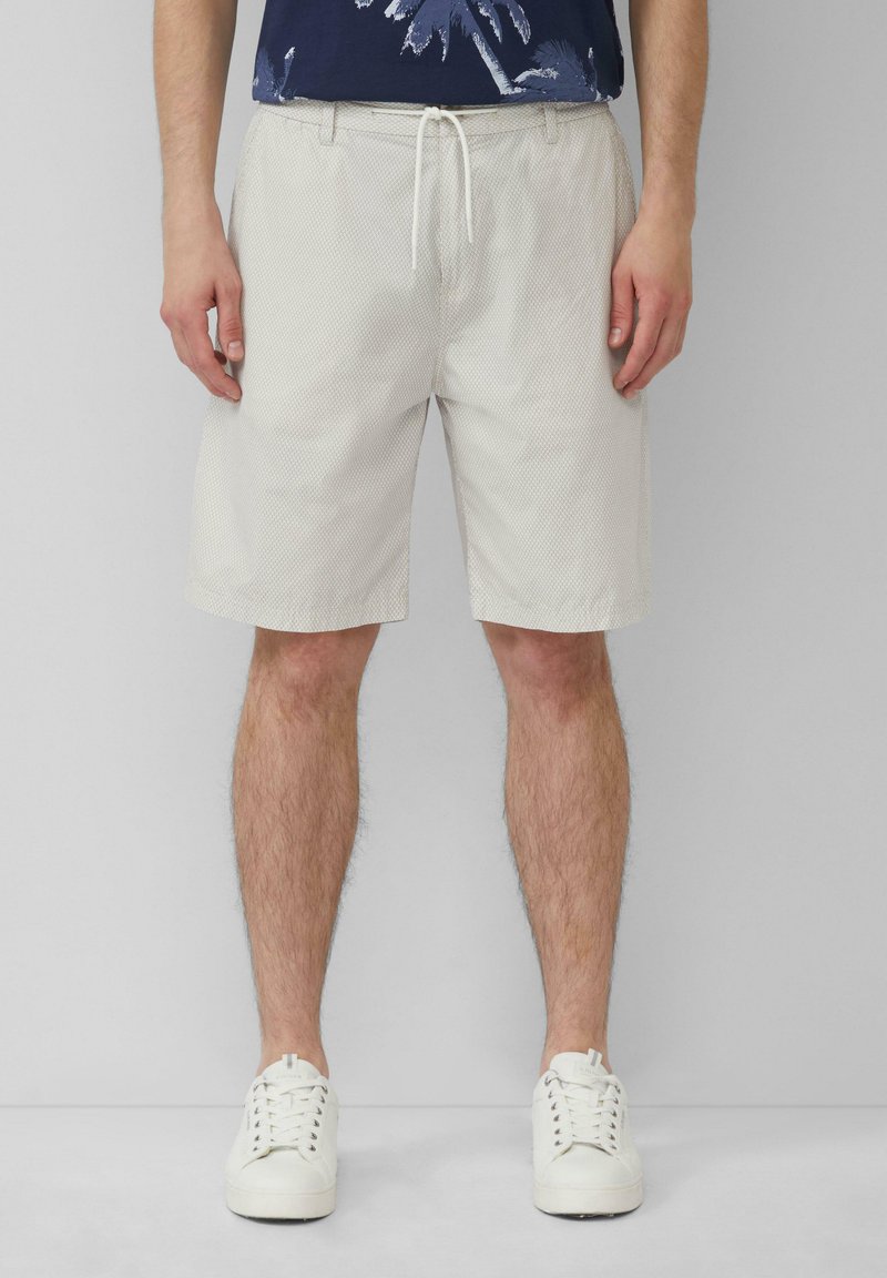 Pantaloni corti grigi chiari a fantasia con cintura elastica, chiusura con cordino e tasche laterali, abbinati a scarpe da ginnastica bianche.