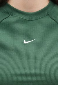 Κοντινό πλάνο ενός ατόμου που φοράει ένα πράσινο ριγωτό μπλουζάκι με το λευκό λογότυπο της Nike στο στήθος.