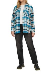 Camicia a quadri con bottoni in blu, nero e bianco, in cotone. Presenta maniche lunghe, una tasca sul petto e una vestibilità comoda. Abbinata a jeans neri.