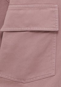 Tkanina w kolorze zasnutego różu z pojedynczą kieszonką na klapę, gładką fakturą oraz skośnym wzorem splotu, z wzmocnionymi detalami stworzonymi ze szwów.