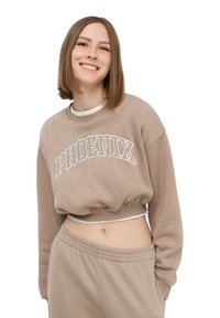 Beżowy krótki sweatshirt z białym napisem "PHOENIX". Posiada długie rękawy i ribbowe wykończenie. Połączony z pasującymi beżowymi spodniami.