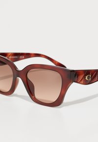 Ochelari de soare tortoiseshell maro cu o formă rectangulară, lentile maro cu degradé și brațe cu un model capitonat, prezentând un accent de logo auriu.