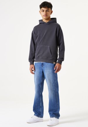 Sudadera de capucha gris oscuro con un bolsillo frontal, combinada con jeans azul claro y zapatillas blancas. La sudadera cuenta con una capucha y puños acanalados.