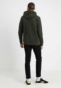 Mörkgrön hoodie med dragsko i huvan, kombinerad med svarta jeans och svarta sneakers med neongröna detaljer. Figursydd design och mjuk textur.