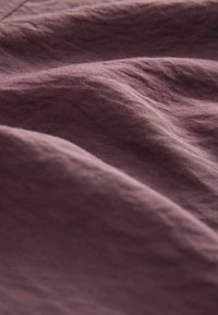 Struktureret stof i dæmpet mauve, der fremviser bløde, bølgede folder. Materialet fremstår let med en subtil glans og milde folder.