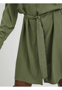 Olivgrön skjortklänning med knytband i midjan, med knappar fram och långa ärmar. Mjuk, slät tygstruktur med avslappnad passform.