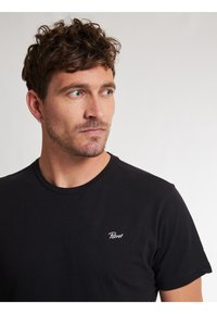 Tricou din bumbac negru cu decolteu rotund și mâneci scurte, având un mic logo alb "Petrol" pe partea stângă a pieptului.