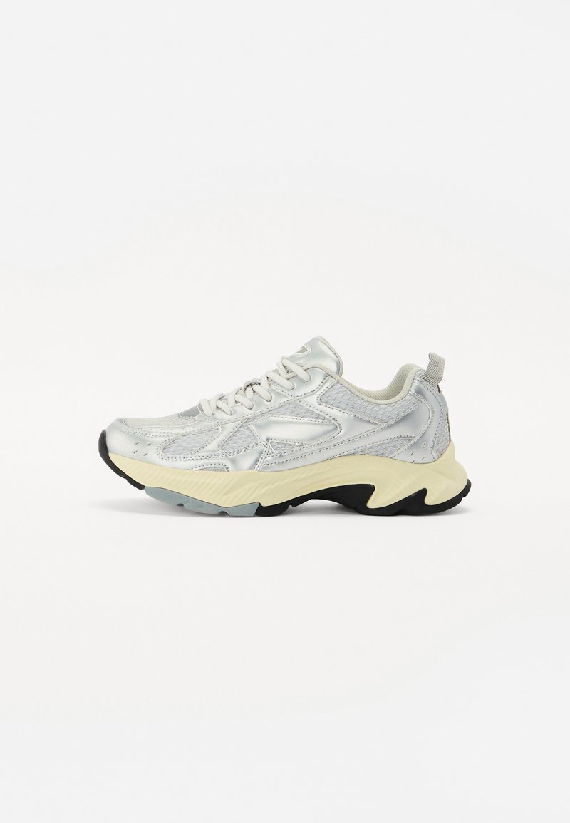 Zilveren sportschoen van mesh en synthetisch materiaal. Chunky zool in crème met een zwarte accent. Voorzien van veters en een lus achteraan.