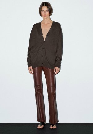 Brown knit cardigan with a V-neck and button closure, paired with brown leather pants. Features a relaxed fit and smooth texture.