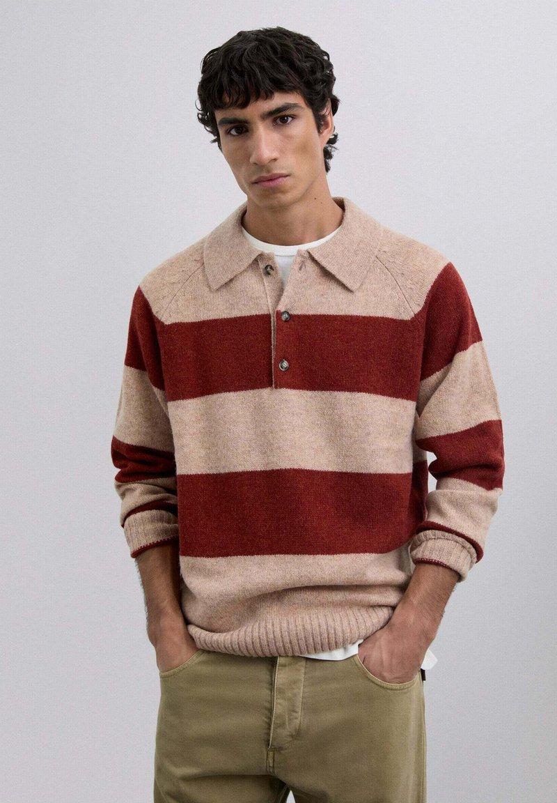 Suéter de punto en beige con llamativas rayas rojas y crema. Cuenta con un cuello, una tapeta de tres botones y puños y dobladillo acanalados.