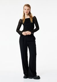 Sort blonde langærmet top med blomstermønstre, parret med højtaljede sorte bukser. Outfittet har et afslappet fit og brede ben.