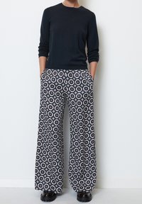 Haut à manches longues bleu marine associé à un pantalon large noir et blanc à motifs avec des accents bleus. Le pantalon dispose de poches latérales et d'une coupe décontractée.