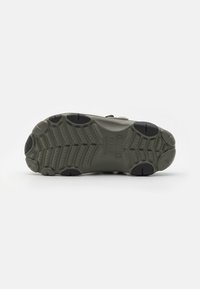 Semelle de chaussure en caoutchouc vert avec un motif texturé, présentant des accents de deux couleurs et des rainures pour une traction. Pas de talon, design plat.