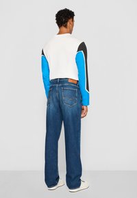 Chemise à manches longues en blocs de couleur avec des panneaux blancs, bleus et noirs ; associée à un jean bleu ample avec poches arrière et étiquette en cuir.