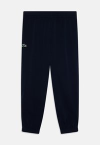 Pantalons de sport bleu marine en tissu doux, avec une taille élastique et des poignets élastiques, arborant un petit logo vert Lacoste sur la jambe gauche.