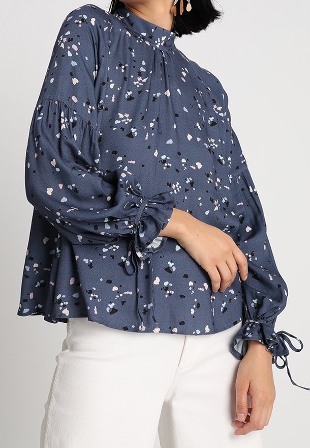 Marinblus med spridda pastell- och svarta abstrakta mönster, hög krage, puffärmar och knytdetaljer vid ärmsluten. Tyg i bomullsblandning.