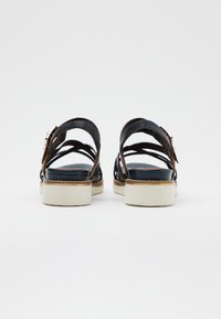 Schwarze Ledersandalen mit überkreuzten Riemen, einer kräftigen beige Sohle und einem metallischen Schnallendetail an der Ferse.