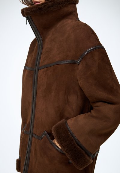 Bruine suède jas met een hoge kraag, bruine fleece voering bij de kraag en manchetten, afgewerkt met contrasterende donkerbruine leren accenten en een ritssluiting.