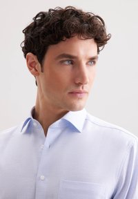 Camicia button-up azzurra chiara realizzata in tessuto testurizzato, con colletto aperto e tasca sul petto lato sinistro.