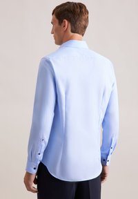 Camicia a maniche lunghe azzurro chiaro con colletto a punta, orlo arrotondato e polsini abbottonati con bottoni oscuri. Tessuto morbido e leggero.