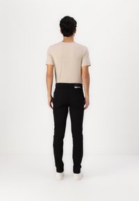 Bež majica s kratkimi rokavi, črne slim-fit kavbojke in bele teniske. Preprost dizajn z gladko teksturo in minimalnimi detajli.