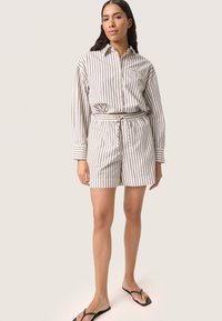 Skjorte med lange ærmer og brystlomme, parret med shorts med bælte. Lavet af et cremet stof med beige lodrette striber.