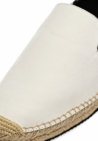 Espadrille en toile blanche avec semelle intermédiaire en jute tressée et semelle extérieure en caoutchouc noir, vue en gros plan de la zone des orteils et du détail des coutures.