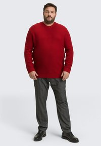 Rode textuurtrui met een ronde hals, gecombineerd met grijze broek en zwarte schoenen. De outfit heeft een ontspannen pasvorm en ribbelmanschetten.
