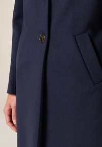 Cappotto in lana blu navy con finitura testurizzata, dotato di chiusura con un solo bottone e tasche laterali per praticità.