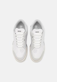 Biele tenisky kombinujúce hladkú kožu a semiš. Obsahujú perforácie pre lepšiu priedušnosť, okrúhle šnúrky a logo na jazyku.