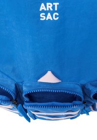 Niebieska torba materiałowa z wieloma zamykanymi kieszeniami, białym napisem "ART SAC" oraz trójkątnym różowym akcentem na górze.
