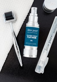 Kollagen-Therapie-Gel in einer blauen und silbernen Pumpflasche, ein silberner Mikronadel-Roller und ein klarer Desinfektionsspray, alles auf einer strukturierten schwarzen Oberfläche.