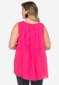 Top senza maniche di un luminoso colore rosa, caratterizzato da un design fluido con schiena arricciata e tessuto morbido e trasparente. Abbinato a jeans scuri.