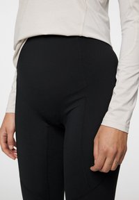 Svarta leggings av elastiskt material, med en åtsittande design och subtila sömdetaljer, tillsammans med en ljusfärgad långärmad tröja.