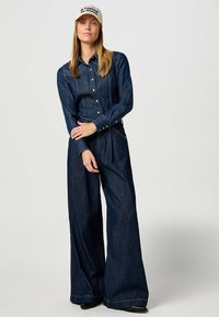 Conjunto de camisa de mezclilla y pantalones de pierna ancha en azul oscuro. La camisa tiene un cierre de botones y cuello; los pantalones tienen una cintura alta y un corte relajado.