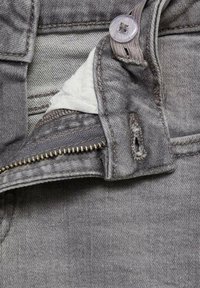 Siva denimski material s prikazano zadrgo, zaponko in notranjo oblogo. Ima obrabljen videz in subtilne podrobnosti šivanja.