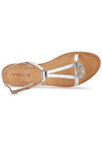 Sandale en cuir argenté avec un design en T, semelle plate et semelle en nude. Caractéristiques d'une finition texturée et d'une bride réglable au niveau de la cheville.